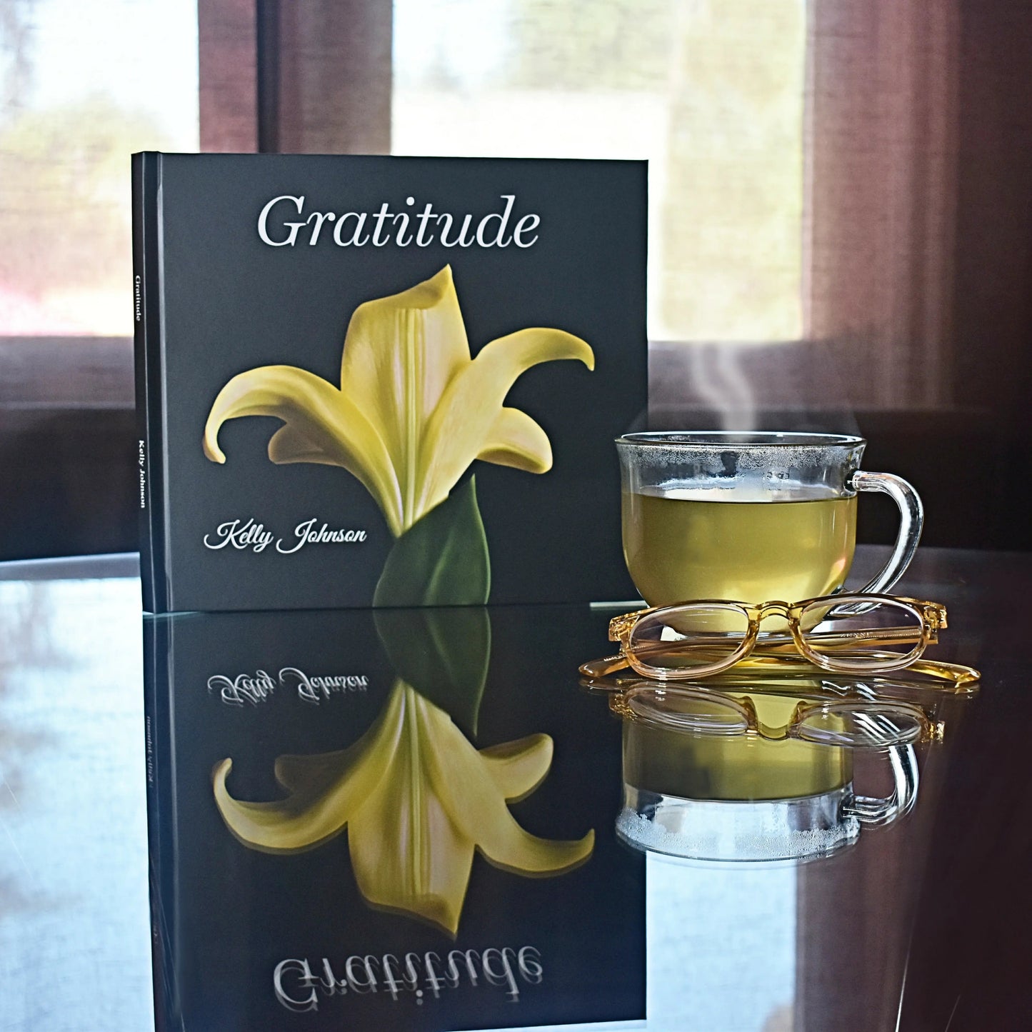 Book cover: Gratitude on a glass table, picture of a yellow lily, tea, and eyeglasses